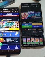 Two smartphones are displayed on a white surface, both showing gambling websites with colorful graphics, text, and various options for logging in and accessing games. The screens are bright and filled with promotional content related to casino and slot games.